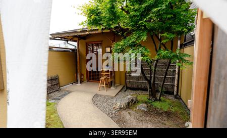 Tranquillo cortile d'ingresso di un tradizionale ristorante giapponese a Tokyo, con cancello in legno, sentiero in pietra, piccolo giardino e albero d'acero. invitante silenzioso Foto Stock