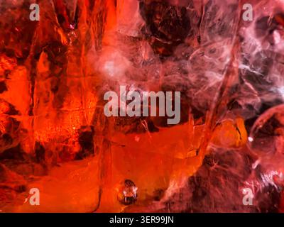 Macro astratto di cubetti di ghiaccio e bolle in un cocktail Aperol, che mostra vivaci tonalità arancio-rosso, riflessi lucidi e freschezza fresca per l'estate dr Foto Stock