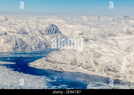 Vista aerea delle montagne artiche innevate, dell'acqua ghiacciata del fiordo, del ghiaccio marino e del paesaggio della calotta ghiacciata della Groenlandia, della Groenlandia meridionale Foto Stock