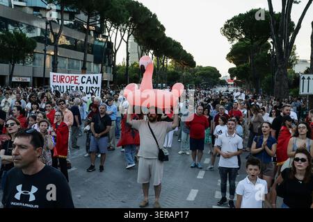 TIRANA, ALBANIA – 17 GIUGNO 2026: Attivisti ambientali, gruppi della società civile, famiglie e giovani prendono parte al diciottesimo giorno consecutivo di manifestazioni contro un progetto di sviluppo del turismo di lusso legato a Jared Kushner. I manifestanti hanno marciato attraverso Tirana centrale portando striscioni, cartelli e bandiere albanesi, chiedendo la cancellazione del progetto e sollevando preoccupazioni circa il suo potenziale impatto ambientale. Le installazioni a tema fenicottero e le esposizioni simboliche sono state rappresentate in modo prominente durante la manifestazione, riflettendo un simbolo crescente del movimento di protesta. Foto di Foto Stock