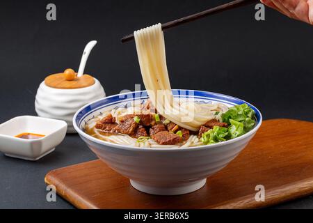 Preparare tagliatelle con bastoncini da una ciotola di zuppa di manzo brasata cinese. Hot Asian Ramen, Food Action Shot. Foto Stock