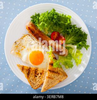 Vista dall'alto delle uova fritte con salsiccia, pane e verdure Foto Stock