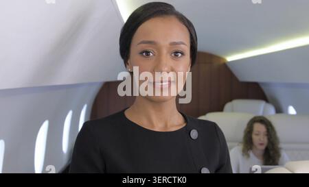 Donna d'affari birazziale in jet privato. Donna imprenditrice africana ben vestita e sicura di sé sorridente all'interno della cabina degli aerei d'affari Foto Stock