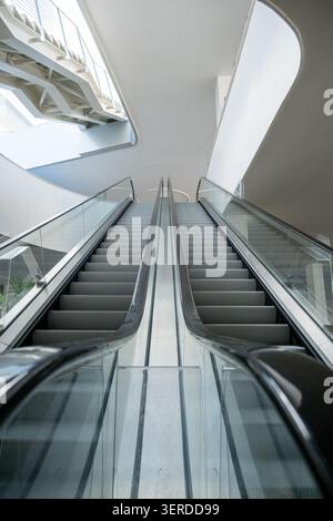 Guarda le scale mobili interne parallele in uno spazio architettonico minimalista, che cattura un'atmosfera pulita e futuristica di connettività urbana e. Foto Stock