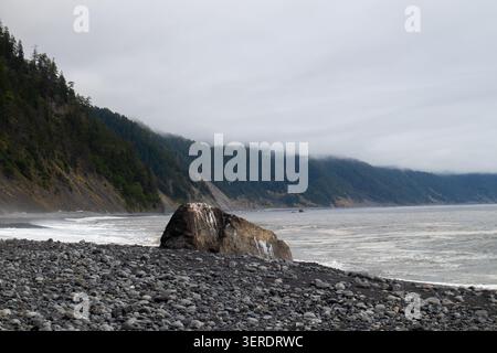 Vista della costa frastagliata di Lost Coast con un grande masso su una spiaggia di ciottoli con colline boscose e l'Oceano Pacifico nella contea di Humboldt Foto Stock