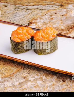 Sushi preparato al momento si siede su un piatto bianco, con salmone e alghe. Il sushi sfoggia colori vivaci su un ripiano in pietra, creando una presentazione appetitosa. Foto Stock