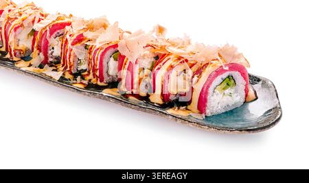 Un lungo piatto contiene diversi sushi roll ripieni di pesce e verdure. I panini sono ricoperti di fiocchi di bonito e un filo di salsa. L'ambiente sembra luminoso e pulito, ideale per gustare il cibo. Foto Stock