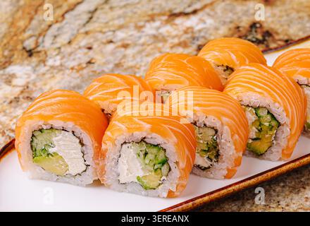 Sushi al salmone fresco poggiato su un piatto bianco. Sono piene di cetriolo e formaggio spalmabile, mostrando colori vivaci in una calda atmosfera da ristorante. Foto Stock