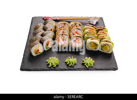 I sushi Rolls sono posizionati su un piatto di pietra nera. Ci sono diversi tipi di sushi, inclusi panini con verdure e pesce. Wasabi è accanto al sushi, insieme alle bacchette. Foto Stock