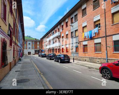EIBAR, SPAGNA - 25 MAGGIO 2025: Una strada tranquilla a Eibar, Spagna, fiancheggiata da edifici in mattoni, auto parcheggiate e lavanderia appesa alle finestre sotto Foto Stock