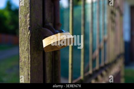 Vista ravvicinata del lucchetto in ottone appeso alla cerniera del cancello in ferro arrugginito, che mostra la consistenza del metallo antico, la patina verde, il muschio e la messa a fuoco superficiale all'aperto Foto Stock