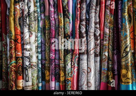 Un primo piano full-frame di una moltitudine di sciarpe colorate di seta o raso appese verticalmente, con elaborati motivi paisley e floreali. Il Foto Stock