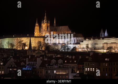 Castello storico illuminato di Praga sopra lo skyline della città di notte, con tetti scuri in primo piano e un cielo nero limpido. Foto Stock