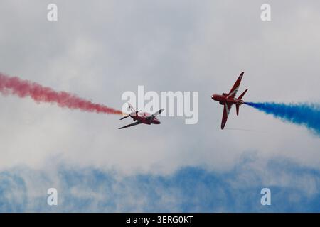 Due getti BAE Hawk rossi brillanti del team di visualizzazione delle frecce rosse della RAF volano in stretta formazione contro un cielo blu nebuloso e nuvoloso. Foto Stock