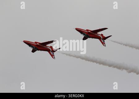Due getti BAE Hawk rossi brillanti del team di visualizzazione delle frecce rosse della RAF volano in stretta formazione contro un cielo blu nebuloso e nuvoloso. Foto Stock