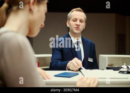 Una receptionist caucasica di mezza età che consegna la chiave elettronica e i documenti a una turista donna compilando i moduli di registrazione al banco del check-in. Servizio di ospitalità, prenotazione di viaggi, concetto di alloggio Foto Stock
