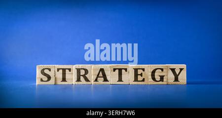 Strategia di ortografia in blocchi di legno su sfondo blu, che simboleggia i concetti di pianificazione, visione aziendale, leadership e successo aziendale. Foto Stock