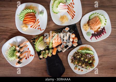 Lo shot sopra la testa presenta sushi assortiti su piatti su superfici in legno. Concentrati su colori vivaci, consistenze di salmone, cetriolo, pesce e riso, con una liscia a Foto Stock