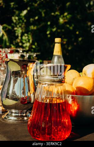 Bevande luminose e frutta fresca sono servite all'aperto durante un raduno durante le ore pomeridiane soleggiate in un giardino. Una ciotola di arance fresche aggiunge colore Foto Stock