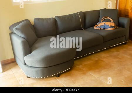 Un ampio divano in tessuto grigio si trova in Una stanza illuminata dal sole, completa di borsa per tutti i giorni appoggiata sui cuscini Foto Stock