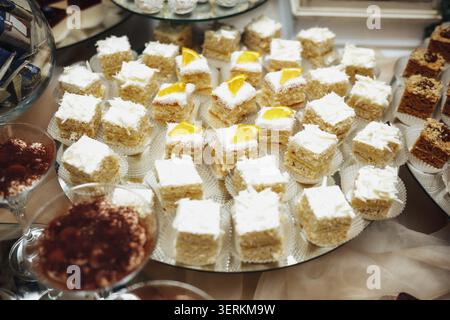 Dolci preparati su un tavolo. Ogni piccola torta condita con panna. Le fette di frutta gialle aggiungono un tocco vibrante. Perfetto per matrimoni, feste o altri eventi Foto Stock