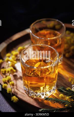 Bicchieri da whisky o Cognac con fiori di Mimosa su vassoio di legno elegante scena di alcol primaverile Foto Stock