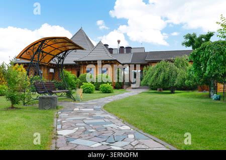 Percorso a mosaico di pietra che conduce alla lussuosa villa in legno attraverso un prato verde. Passerella decorativa in pietra ammiraglia in un giardino paesaggistico professionale Foto Stock