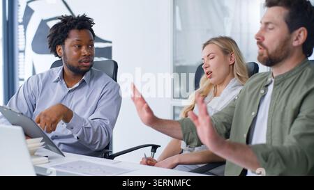 Gruppo di affari internazionale di tre lavoratori che discutono problemi di carta boss afroamericano mostrando cartella tablet con dati documento uomo caucasico Foto Stock
