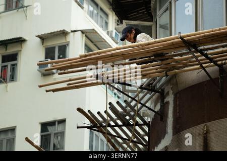 Un lavoratore dispone pali per impalcature di bambù su un piano superiore di un vecchio edificio residenziale a Mong Kok, Kowloon, Hong Kong Foto Stock