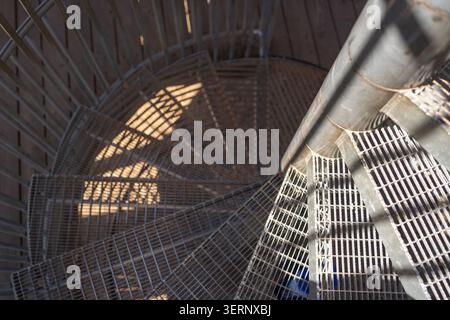 Scenografica scala a spirale in metallo per esterni a contrasto elevato. La luce solare intensa crea forti ombre grafiche sui gradini della griglia in acciaio Foto Stock