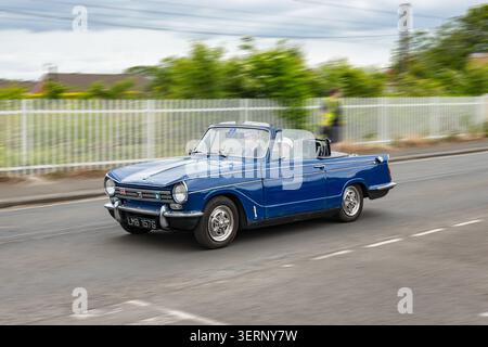 Auto d'epoca convertibile Blue Triumph Herald che guida su una strada nel Regno Unito con movimento sfocato Foto Stock