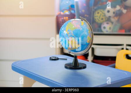 Modello di mappa del globo con lente d'ingrandimento su una scrivania per bambini di studio nella sala giochi. Simboleggia l'esplorazione globale e l'educazione dei bambini Foto Stock