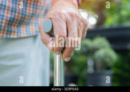 Bastone da passeggio, mano e anziano nel giardino di casa con demenza in una struttura di cura per malattia. Concetto di bastone da passeggio e assistenza sanitaria. Foto Stock