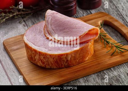 Prosciutto affumicato a fette su tavola di legno con ramoscio di rosmarino e macinapepe. Concetto di cibo proteico sano Foto Stock