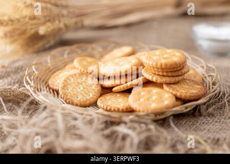 Cracker rotondi salati su piatto di vimini con fondo rustico da cucina e frumento Foto Stock