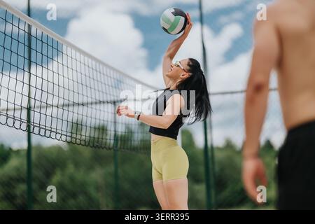 Una giovane atleta che punta a pallavolo su rete durante una partita estiva all'aperto Foto Stock