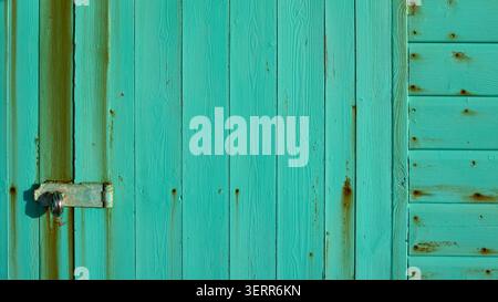 La struttura delle porte in legno turchese resistente agli agenti atmosferici presenta una serratura arrugginita e bulloni sulla porta hutt della spiaggia, creando uno sfondo rustico Foto Stock