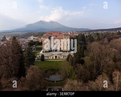 Vista aerea dello storico Castello Duca di Aglie con la sua grande facciata e lo stagno circolare nel parco sullo sfondo di una montagna Aglie, Piemonte, Italia. Foto Stock