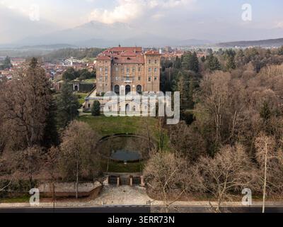 Veduta aerea del Castello Duca delle Aglie con la sua storica facciata in mattoni, i giardini formali e la fontana circolare sotto un cielo morbido ad Aglie, Piemonte, Italia. Foto Stock