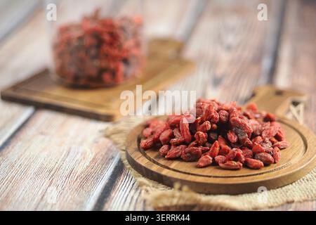 Bacche di goji su un asse con un barattolo dietro Foto Stock