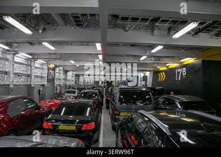Affollato ponte interno di un traghetto per auto commerciali che attraversa la Manica. L'auto rossa e le altre auto sono parcheggiate bene Foto Stock