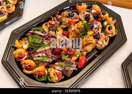 Stuzzichini gourmet assortiti con salmone affumicato, gamberi, affettati, frutti di bosco ed erbe aromatiche su un vassoio catering per eventi e ricevimenti. Foto Stock