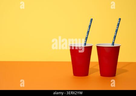Occhiali di plastica rossi con cannucce blu su sfondo giallo. Foto Stock