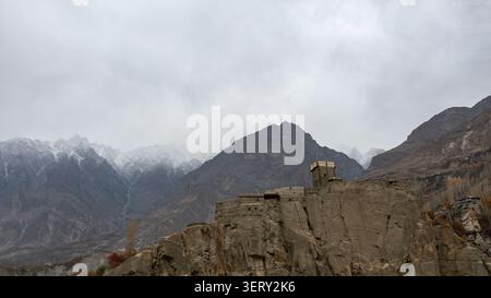 Vista aerea del forte di Altit arroccato su una scogliera rocciosa con montagne innevate sullo sfondo sotto un cielo nuvoloso ad Altit, Gilgit, Pakistan. Foto Stock