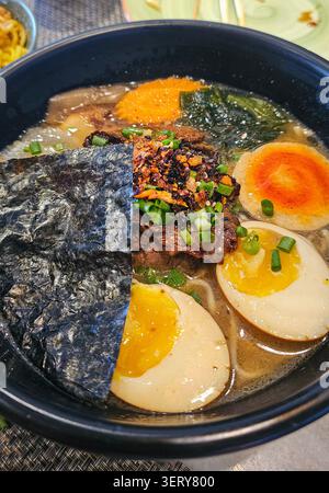 Delizioso ramen giapponese con manzo, uova sode, alghe nori, funghi e cipollotti freschi in un brodo saporito. Zuppa tradizionale di noodles asiatici Foto Stock