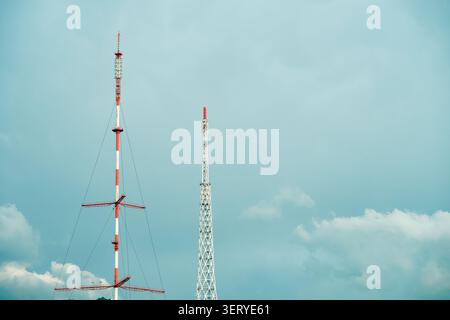 I trasmettitori di segnale dei telefoni cellulari industriali e le antenne di trasmissione si avvicinano. Due diverse torri di telecomunicazione e montanti radio contro il nuvoloso Foto Stock