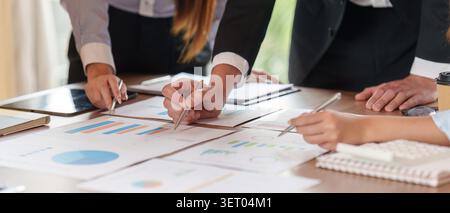 Team aziendale diversificato che esamina grafici e report finanziari, discute di strategia e dati economici in un ambiente di ufficio moderno. Concentrarsi sulla collaborazione e sul lavoro analitico. Foto Stock