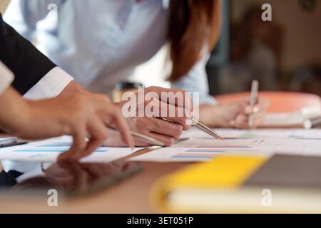 Team aziendale diversificato che esamina grafici e report finanziari, discute di strategia e dati economici in un ambiente di ufficio moderno. Concentrarsi sulla collaborazione e sul lavoro analitico. Foto Stock