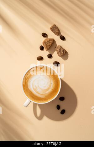 Tazza di caffè, schiuma per cappuccino e zucchero di canna su sfondo colorato con ombra dura. Vista dall'alto, primo piano, immagine verticale. Foto Stock