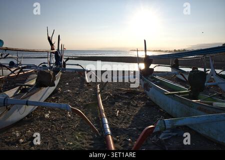 Barche tradizionali a bilanciere in legno parcheggiate su una costa rocciosa di fronte a un tramonto luminoso sull'oceano a Bali. Foto Stock